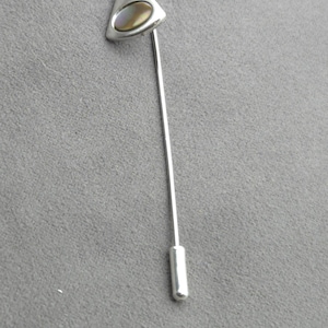 May include: A silver-toned lapel pin featuring a triangular head with a smooth, polished finish. An oval-shaped, iridescent shell inlay is set into the center of the triangular head. The pin includes a long, slender metal stem and a cylindrical end cap.