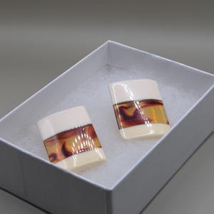 May include: A pair of rectangular earrings featuring a smooth, cream-colored finish with a central horizontal band of brown and amber tortoiseshell-style pattern. The earrings are presented inside a white box with a soft, white interior lining.