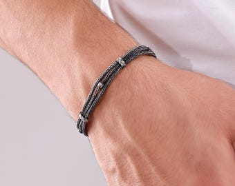 May include: A silver-toned bracelet with a braided design. The bracelet features three strands of woven metal, with small decorative knots and beads. The jewelry is worn on the wrist.
