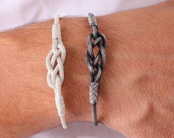 May include: Two silver-colored bracelets with intricate knot designs. One bracelet is a lighter silver, while the other is a darker, oxidized silver. The bracelets are displayed on a person's arm, showcasing their detailed craftsmanship.