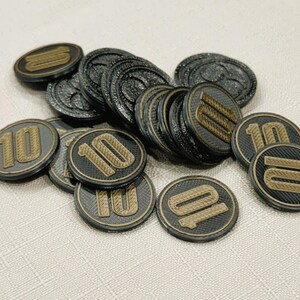 A pile of silver, circular game coins worth ten coins. The coins have a raised "10" on the front and a submerged symbol on the back. These premium board game coins replace the standard card board coins.