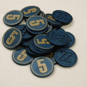 A pile of metallic blue, circular game coins worth five coins. The coins have a raised "3" on the front and a submerged symbol on the back. These premium board game coins replace the standard card board coins.