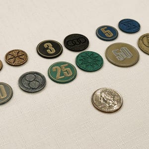Generic Board game coins with various denominations, including 1, 3, 5, 10, 25 and 50. The coins feature various designs, including numbers, symbols, and logos, in colors like gold, green, black, and blue. A quarter is provided for scale.