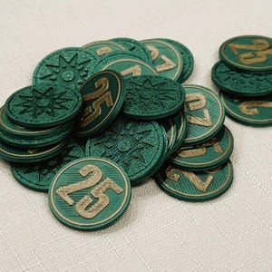 A pile of metallic green, circular game coins worth twenty five coins. The coins have a raised "25" on the front and a submerged symbol on the back. These premium board game coins replace the standard card board coins.