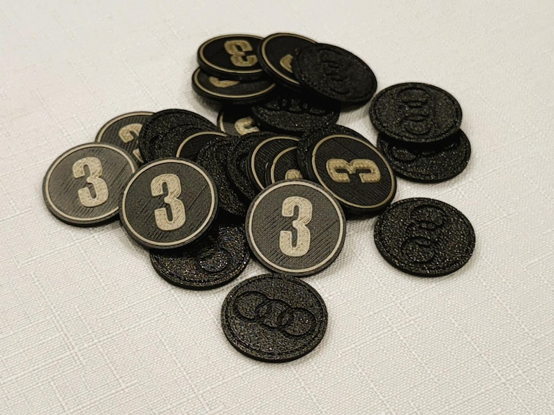 A pile of iron gray, circular game coins worth three coins. The coins have a raised "3" on the front and a submerged symbol on the back. These premium board game coins replace the standard card board coins.