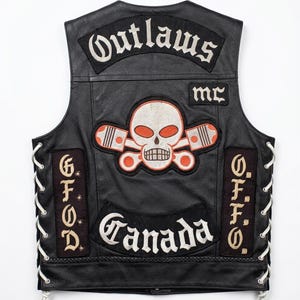 Peut inclure: Un gilet en cuir noir avec un laçage blanc sur les côtés. Le dos présente des écussons brodés incluant le texte Outlaws, MC et Canada, ainsi qu'un motif central représentant un crâne avec deux pistons croisés en blanc et orange.