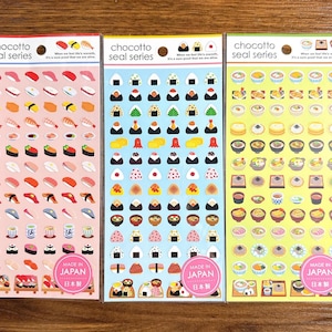 Puede incluir: Tres hojas de pegatinas de la "chocotto seal series" con ilustraciones coloridas de sushi, onigiri y sopa japonesa. Cada hoja tiene un color de fondo diferente: rosa, azul y amarillo. El texto "MADE IN JAPAN" es visible en cada hoja.