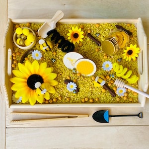 Peut inclure: Un plateau en bois rempli de riz jaune, de tournesols et de jouets sur le thème des abeilles. Comprend une cuillère en bois, un pot à miel et une petite pelle. Éléments décoratifs : abeilles en feutre, marguerites et pot de miel. Un ensemble de jeu sensoriel amusant.