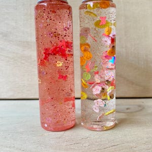 Può includere: Un set di tre tazze in ceramica con smalto screziato color crema. Ogni tazza presenta un diverso motivo floreale dipinto a mano nei toni del blu, verde e giallo. Le tazze hanno una forma semplice e arrotondata e un manico.