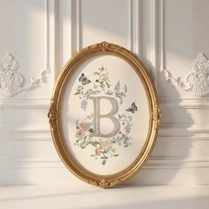 Può includere: Un'opera d'arte ovale con cornice dorata, raffigurante la lettera "B" circondata da motivi floreali e farfalle. L'opera ha uno sfondo color crema ed è esposta su una parete bianca con modanature decorative.