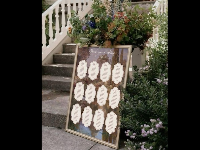 May include: A framed seating chart with the text "Find your Seat" displayed at an outdoor wedding. The chart features several individual name cards with decorative borders. The background shows a landscape scene with trees and a staircase.