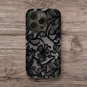 Peut inclure: Coque de téléphone noire et grise avec un motif de dentelle florale. Le boîtier a une finition brillante et une découpe pour l'appareil photo. Le motif présente des motifs floraux complexes et une texture délicate et dentelée.
