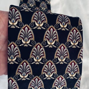 May include: A black necktie featuring a repeating pattern of pointed, arch-shaped motifs. Each motif contains layered, fan-like segments in shades of burgundy, grey, and cream, outlined in gold, with a small blue accent at the base of each design.