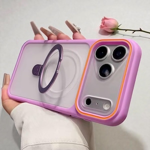 May include: A lilac phone case with a clear back and a built-in ring holder. The case has an orange border around the camera section. The ring holder is purple. The case is designed to protect the phone.