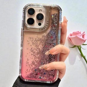 May include: Clear phone case with a liquid and glitter design. The case has a gradient of pink and clear liquid with floating glitter. The case has a clear bumper and a camera cutout. The text "SHS CASE" is visible.