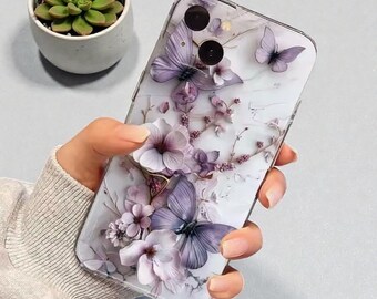 May include: A clear phone case with a 3D floral design. It features lavender butterflies and flowers against a marble-effect background. The case is held in a hand. A small succulent plant in a white pot is visible in the background.