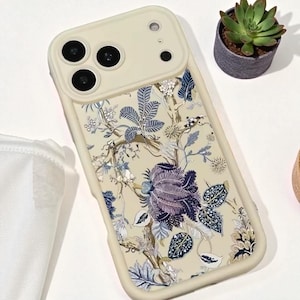 May include: A cream-colored phone case with a floral design. The case features a pattern of blue, purple, and cream-colored flowers and leaves. The case has a raised camera section and a cream-colored border.