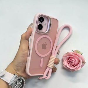 May include: A pink phone case with a matching lanyard. The case has a clear back and a pink frame, with a circular design and the Apple logo. The lanyard is made of a pink rope material. A pink rose is next to the phone.