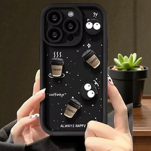 May include: Black phone case with a whimsical design featuring coffee cups, cartoon characters, and the words "caffeine" and "ALWAYS HAPPY". The case has a matte finish and a raised design.