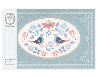 May include: A rectangular message card with a blue border featuring a scalloped edge. The center displays an oval with two blue birds, pink and blue flowers, and green leaves. The text Antik Piac and Japanese characters are printed on the left side.