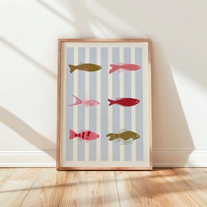 Pode incluir: Uma impressão artística emoldurada com seis ilustrações de peixes coloridos em um fundo listrado azul claro e branco. Os peixes são em tons de rosa, vermelho, verde e dourado. A moldura é de madeira clara.