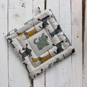 May include: A beige pot holder with a pattern of black, white, and yellow dogs. The dogs are in various poses, including sitting, standing, and running.