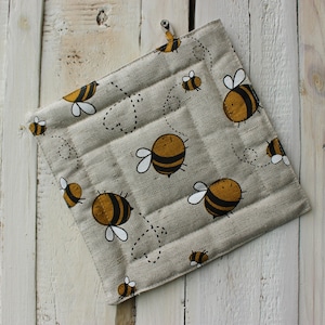 Peut inclure: Un dessous de plat en lin beige avec un motif matelassé et un motif d'abeilles jaunes et noires.