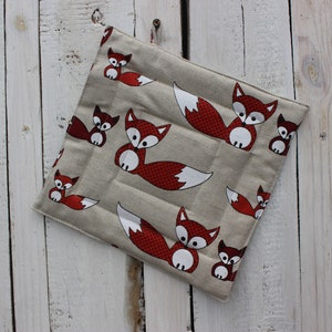 Peut inclure: Un dessous de plat carré matelassé en tissu beige clair avec un motif répétitif de renards stylisés rouges et blancs aux contours noirs. Le dessous de plat possède une petite boucle en tissu dans le coin supérieur pour le suspendre.