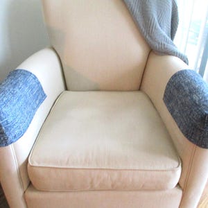 May include: A white armchair with blue fabric armrest covers. The chair has a light beige fabric upholstery and a simple design.