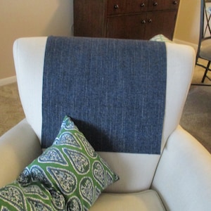 May include: A white armchair with a blue fabric panel on the back. A green and blue paisley patterned pillow rests on the seat. The chair is in a well-lit room.