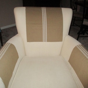 May include: A white armchair with brown and white striped fabric armrests and back. The chair has a tufted back and a white fabric seat.