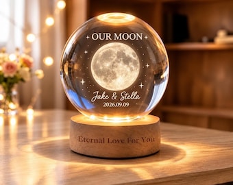 May include: A spherical glass lamp featuring an internal laser-etched moon and stars. The text reads OUR MOON, Jake & Stella, and 2026.09.09. The glass sphere rests on a cylindrical wooden base engraved with the text Eternal Love For You.