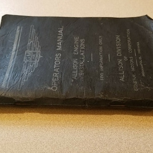 May include: A vintage black Operators Manual for Allison Engine Installations. The cover features the GM Air Power logo and text indicating it's from the Allison Division of General Motors Corporation, Indianapolis, Indiana. The manual appears worn, suggesting age and use.