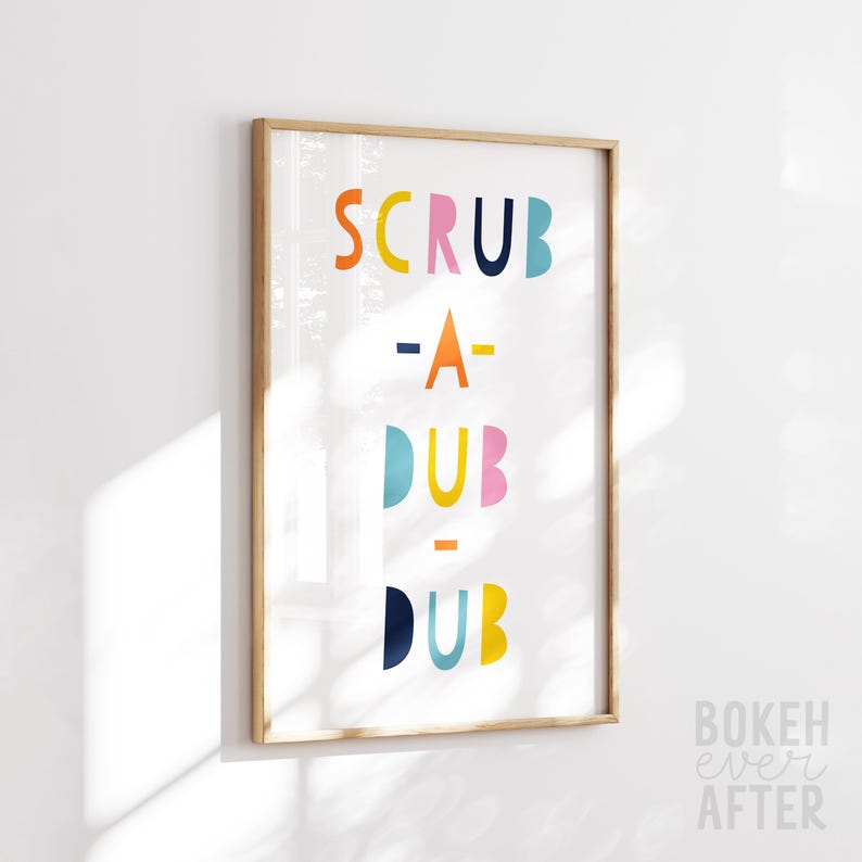 May include: A rectangular wall art print in a light wood frame featuring the text SCRUB-A-DUB-DUB in colorful, rounded, sans-serif letters. The letters are arranged in four lines with orange, yellow, pink, dark blue, and light blue colors.