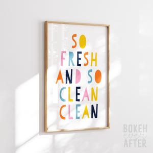 May include: A rectangular wall art print in a light wood frame featuring the text SO FRESH AND SO CLEAN CLEAN in a multi-colored, sans-serif font. The letters are rendered in shades of yellow, orange, pink, light blue, and dark navy blue.