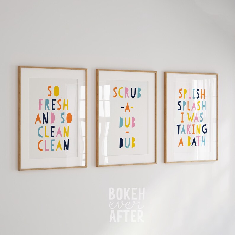May include: Three framed wall art prints with light wood frames. The first print reads SO FRESH AND SO CLEAN CLEAN, the second reads SCRUB-A-DUB-DUB, and the third reads SPLISH SPLASH I WAS TAKING A BATH in colorful, bold, sans-serif lettering.