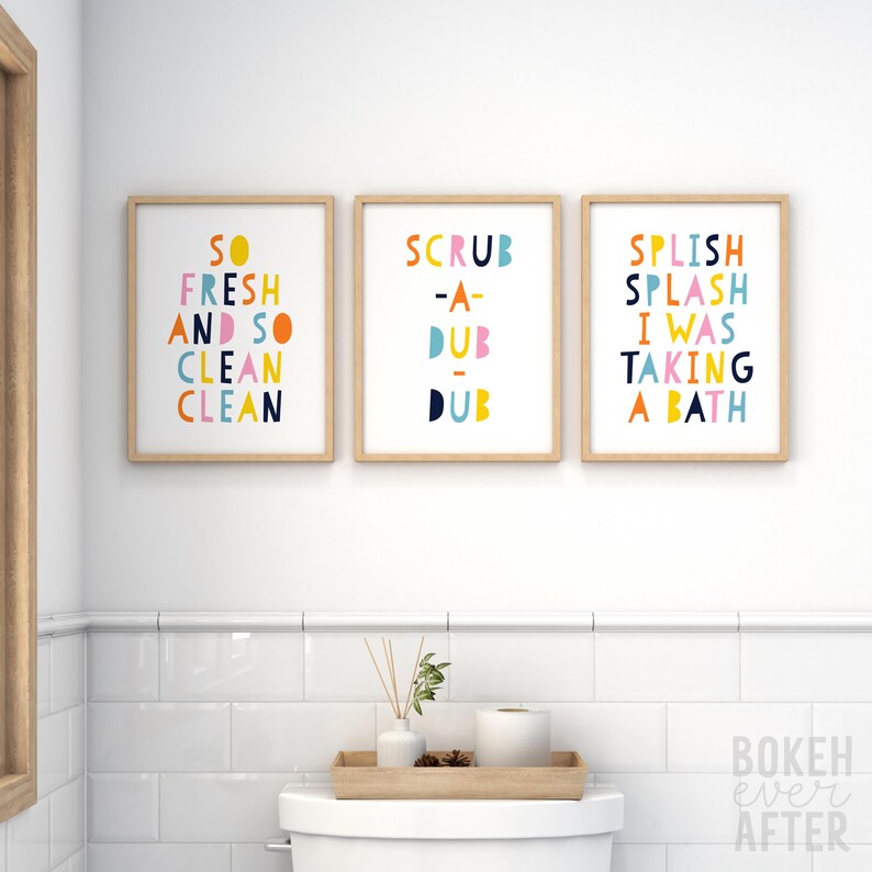 May include: Three rectangular wall art prints in light wood frames. The first print reads SO FRESH AND SO CLEAN CLEAN, the second reads SCRUB-A-DUB-DUB, and the third reads SPLISH SPLASH I WAS TAKING A BATH in colorful, rounded, sans-serif lettering.