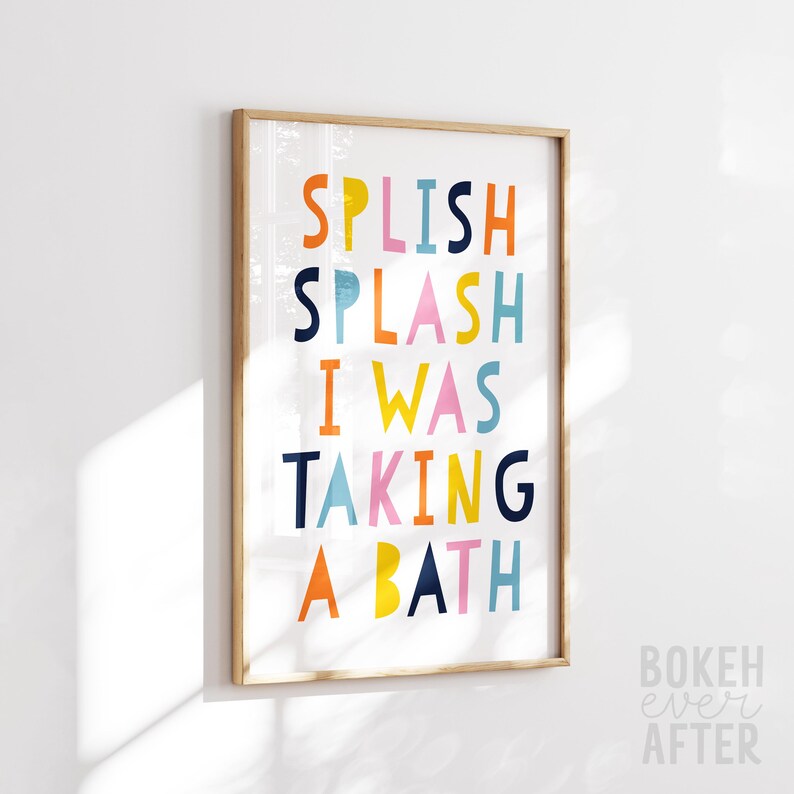 May include: A rectangular wall art print in a light wood frame featuring the colorful text SPLISH SPLASH I WAS TAKING A BATH in shades of orange, yellow, pink, light blue, and dark blue against a white background, displayed in a vertical orientation.