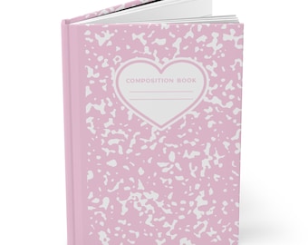 Könnte beinhalten: Ein Notizbuch mit festem Einband und einem hellrosa-weißen Sprenkelmuster. Auf dem Vorderdeckel befindet sich ein weißes, herzförmiges Etikett mit rosa Rand, das den Text COMPOSITION BOOK und zwei horizontale Linien zum Beschriften enthält.