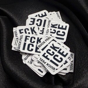K&ouml;nnte beinhalten: Ein Haufen wei&szlig;er quadratischer Aufkleber mit den Worten "FCK ICE" in fetten schwarzen Buchstaben. Die Worte "QUICK PEEL" sind auf der Seite jedes Aufklebers aufgedruckt. Auf schwarzem Hintergrund.