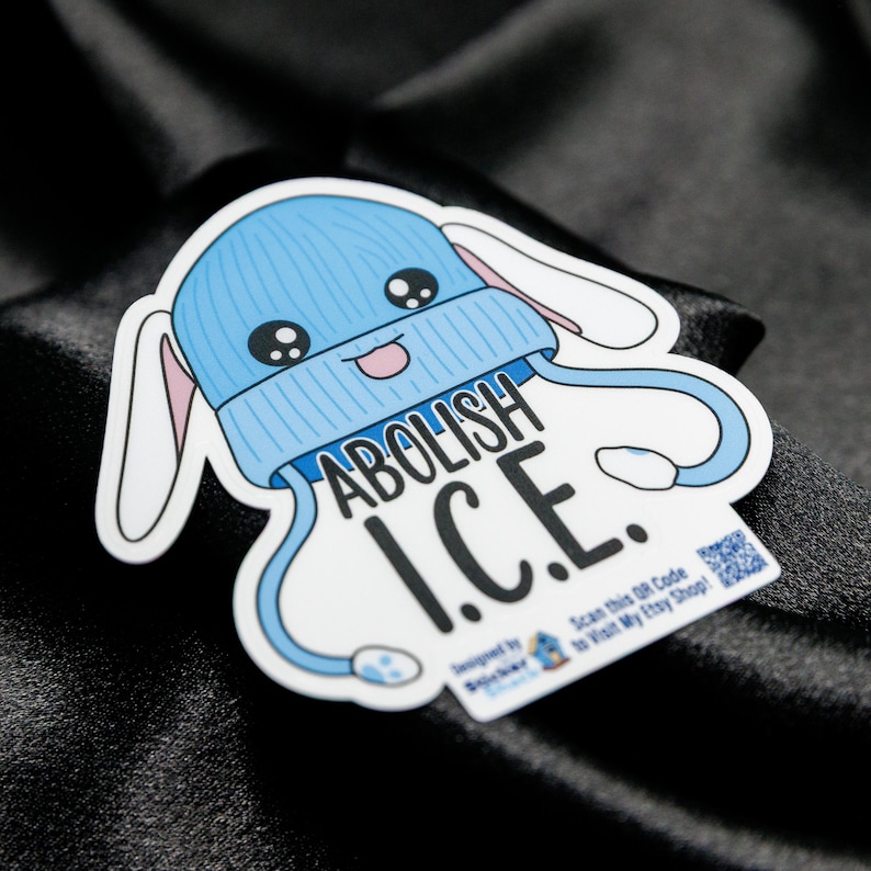 May include: A sticker featuring a cartoon bunny wearing a light blue beanie with the words "ABOLISH I.C.E." The sticker has a white border and a QR code. The bunny has large eyes and a smiling mouth.