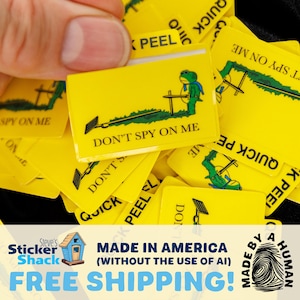 May include: A rectangular yellow sticker featuring a green frog character holding a sword, standing on a patch of grass. The text DON'T SPY ON ME is printed in black below the graphic. The sticker has a tab at the top labeled QUICK PEEL.