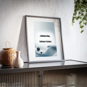 May include: A framed print featuring the text "Software Bug" and "Software Feature" over a light blue and white abstract design. A black sphere and a spider graphic are also visible. The frame is dark grey, displayed on a dark cabinet.