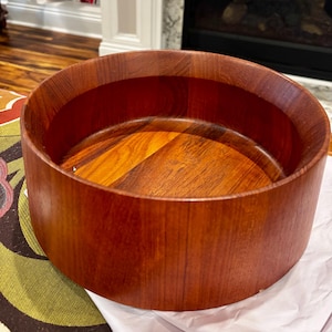 May include: A round, wooden salad bowl with a rich, reddish-brown finish. The bowl has a wide, cylindrical shape with a smooth interior and exterior. The wood grain is visible, adding to its natural aesthetic. The bowl is empty and ready for use.