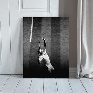 Puede incluir: Impresión en blanco y negro de un tenista sacando en una cancha. El jugador está en pleno servicio, con la raqueta levantada, con las líneas de la cancha y la red visibles. La imagen enmarcada se apoya en una puerta blanca y un suelo de madera.