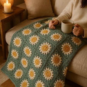 May include: A crocheted blanket with a daisy pattern in sage green, cream, and yellow. The blanket is displayed on a sofa. The daisy design is repeated across the blanket, creating a textured and visually appealing textile.