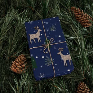 May include: A wrapped gift with navy blue wrapping paper featuring a pattern of reindeer, snowflakes, and Christmas trees. The gift is tied with twine and set against a backdrop of pine needles and pine cones.