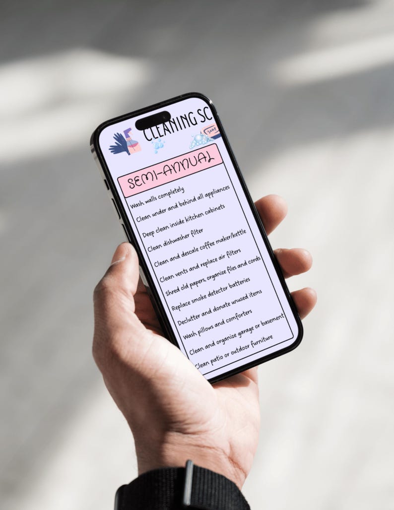 May include: A smartphone screen shows a semi-annual cleaning schedule. The list includes tasks such as washing walls, cleaning appliances, and decluttering. The phone is held in a hand, with the text in black against a white background.
