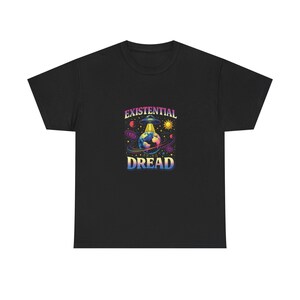 Puede incluir: Camiseta negra con un gráfico colorido que presenta un OVNI, la Tierra, el sol y planetas. El texto "EXISTENTIAL DREAD" se muestra en una fuente de gradiente arcoíris. Esta prenda informal tiene un diseño vibrante y llamativo.