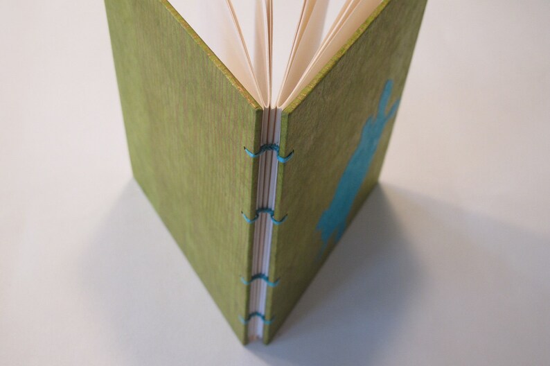 Pu&ograve; includere: Un diario verde con un design a silhouette blu sulla copertina. Il diario &egrave; rilegato con filo blu e ha un interno color crema.